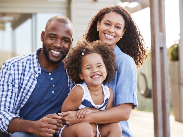 Young black family embracing outdoors and smiling at camera